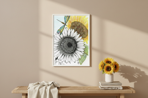 Sunflowers and Dragonfly art print in a white frame on a warm neutral wall above a wooden bench with fresh sunflowers and a linen throw